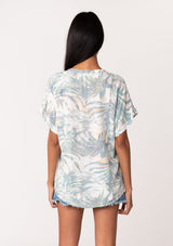 [Color: Natural/Seafoam] A back facing image of a brunette model wearing a lightweight summer tee in a green palm leaf print. With short cuffed sleeves, a v neckline, and a relaxed fit. 