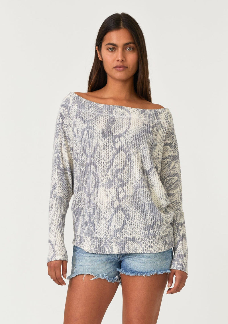 [Color: Light Grey/Ivory] A half body front facing image of a brunette model wearing a soft waffle knit pullover top in a grey and ivory snakeskin print. With long tapered dolman sleeves and a wide neckline that can be worn on or off the shoulder.