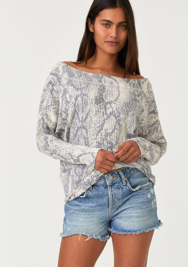 [Color: Light Grey/Ivory] A front facing image of a brunette model wearing a soft waffle knit pullover top in a grey and ivory snakeskin print. With long tapered dolman sleeves and a wide neckline that can be worn on or off the shoulder. 
