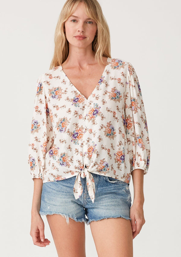 [Color: Natural/Rust] A front facing image of a blonde model wearing a best selling tie front blouse in a white and pink floral print. With three quarter length sleeves, a v neckline, and a relaxed fit. 