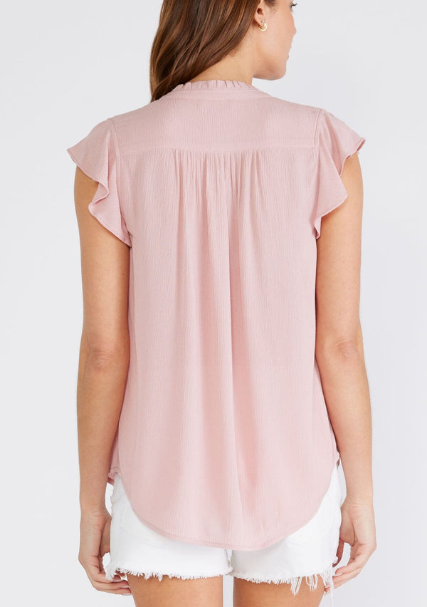 [Color: Dusty Pink] A back facing image of a brunette model wearing a soft pink crinkle gauze short sleeve flutter top with a button front and a ruffled neckline.