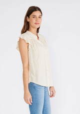 [Color: Natural] A side facing image of a brunette model wearing an off white crinkle gauze short sleeve flutter top with a button front and a ruffled neckline.