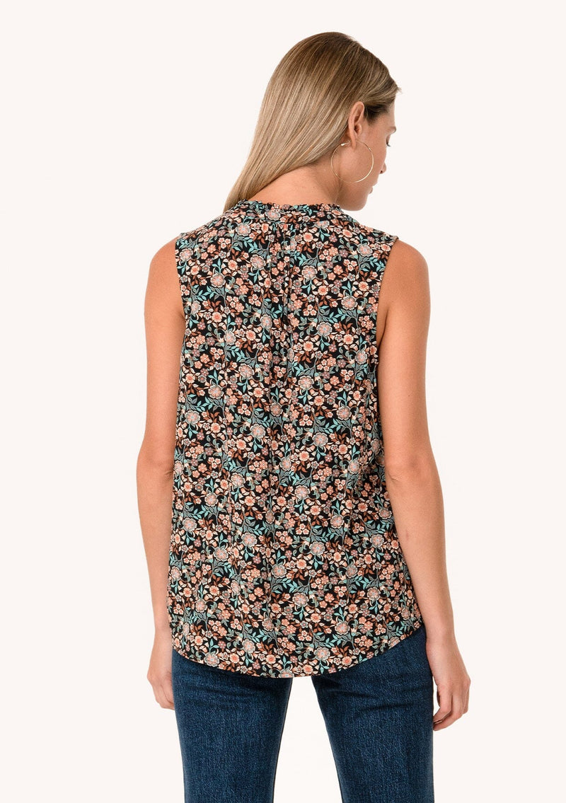 [Color: Black/Teal] A back facing image of a blonde model wearing a transitional fall sleeveless blouse in a black and teal floral print. With a button front, a ruffle trimmed neckline, and a relaxed fit. 