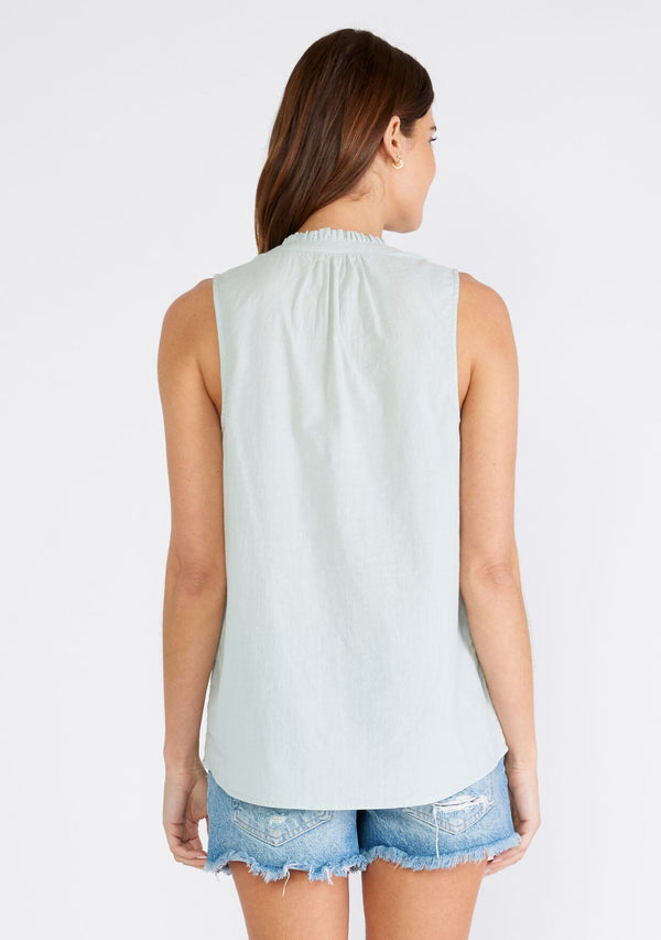 [Color: Dusty Seafoam] A back facing image of a brunette model wearing a sleeveless spring top in dusty seafoam. With a ruffle trimmed round neckline, a button front, and a relaxed fit. 