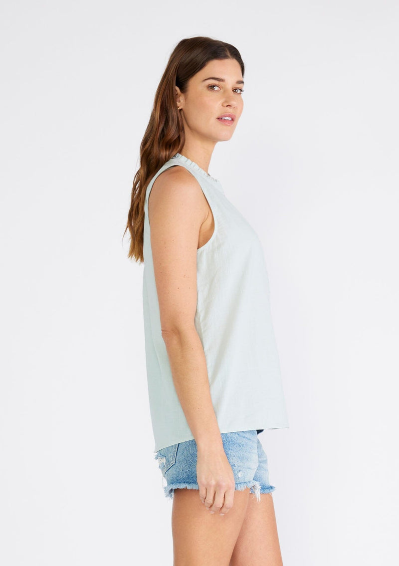 [Color: Dusty Seafoam] A side facing image of a brunette model wearing a sleeveless spring top in dusty seafoam. With a ruffle trimmed round neckline, a button front, and a relaxed fit. 