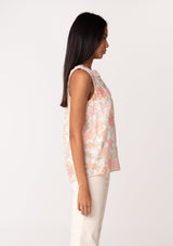 [Color: Natural/Coral] A side facing image of a brunette model wearing a lightweight cotton tank top in a pink floral print. With a ruffled neckline, a button front, and a relaxed fit. 
