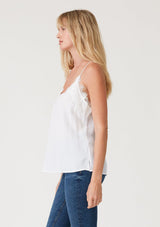[Color: Chalk] A side facing image of a blonde model wearing a white lace trim camisole with a v neckline, adjustable spaghetti straps, and a flowy relaxed fit.