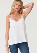[Color: Chalk] A front facing image of a blonde model wearing a white lace trim camisole with a v neckline, adjustable spaghetti straps, and a flowy relaxed fit.