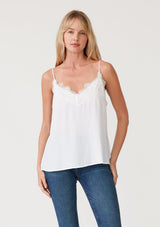 [Color: Chalk] A front facing image of a blonde model wearing a white lace trim camisole with a v neckline, adjustable spaghetti straps, and a flowy relaxed fit.