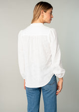 [Color: White] A back facing image of a blonde model wearing a classic bohemian cotton white button front shirt in a textured jacquard. With long sleeves and a ruffled neckline.