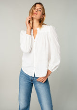 [Color: White] A front facing image of a blonde model wearing a classic bohemian cotton white button front shirt in a textured jacquard. With long sleeves and a ruffled neckline.
