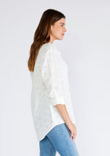 [Color: White] A side facing image of a brunette model wearing a classic white bohemian shirt crafted in embroidered eyelet cotton. With long sleeves, a classic collared neckline, and a button front. 