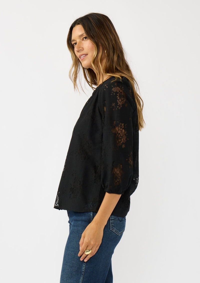 [Color: Black] A side facing image of a brunette model wearing a black lace blouse with a button front, split v-neckline and 3/4 length sleeves. A classic and romantic top for the fall season. 