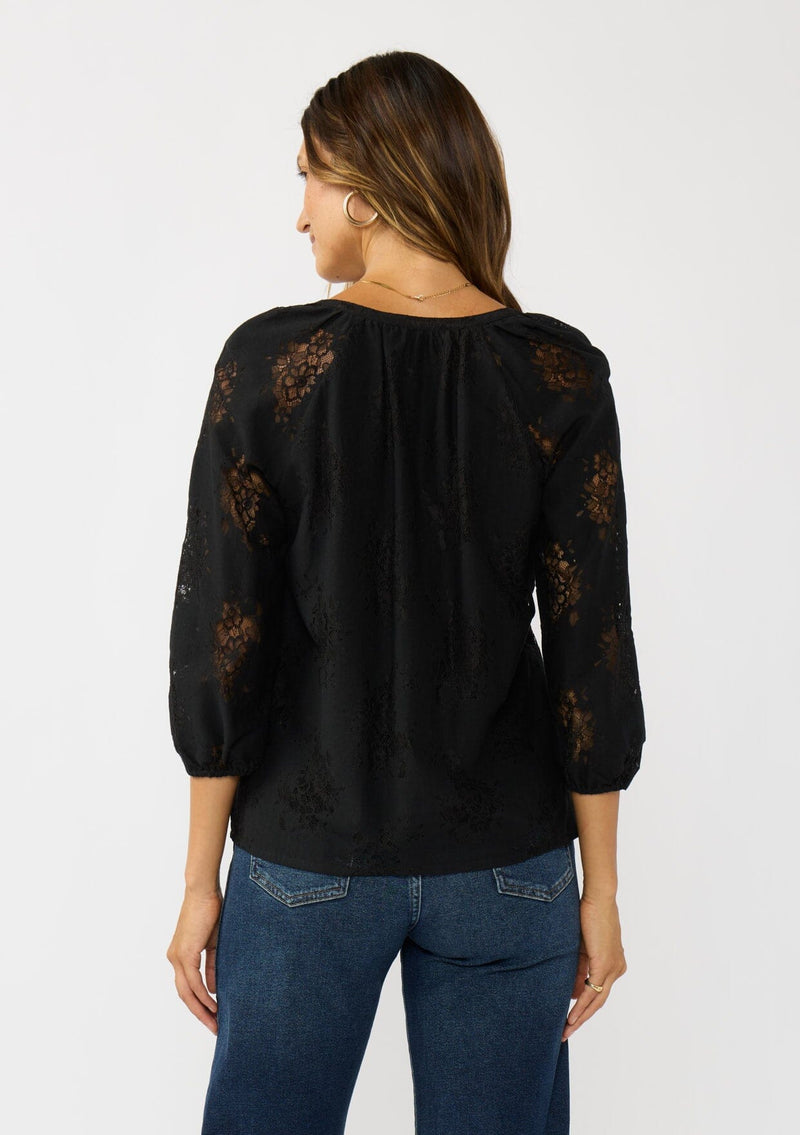 [Color: Black] A back facing image of a brunette model wearing a black lace blouse with a button front, split v-neckline and 3/4 length sleeves. A classic and romantic top for the fall season. 