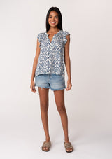 [Color: Ivory/Denim] A front facing image of a brunette model wearing a casual bohemian blouse in a blue bohemian diamond print. With short ruffle sleeves, a v neckline, and a relaxed fit. 