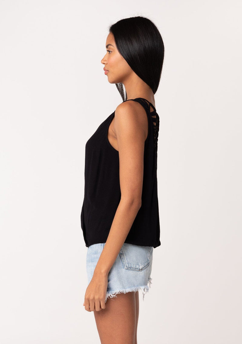 [Color: Black] A side facing image of a brunette model wearing a casual black bohemian summer tank top with a surplice v neckline, an elastic waist, and a back soutache braided detail. 