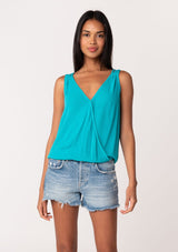 [Color: Turquoise] A front facing image of a brunette model wearing a casual turquoise blue bohemian summer tank top with a surplice v neckline, an elastic waist, and a back soutache braided detail. 