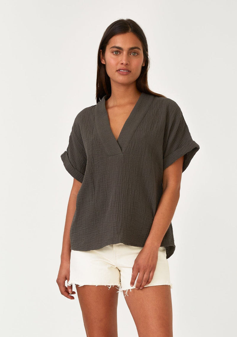 [Color: Lagoon] A half body front facing image of a brunette model wearing an olive green cotton gauze tee. With short cuffed sleeves, a v neckline, and an oversized relaxed fit. 
