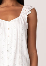 [Color: White] A close up front facing image of a brunette model wearing a white summer top with embroidered eyelet details. With a button front, flutter straps, and a scoop neckline. 