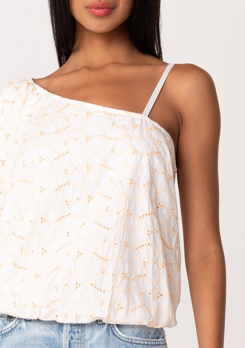 [Color: White/Apricot] A close up front facing image of a brunette model wearing a lightweight cotton summer blouse in a white and pink embroidered design. With a one shoulder asymmetric neckline, a short puff sleeve, an adjustable spaghetti strap, and a relaxed fit. 