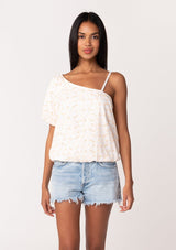 [Color: White/Apricot] A front facing image of a brunette model wearing a lightweight cotton summer blouse in a white and pink embroidered design. With a one shoulder asymmetric neckline, a short puff sleeve, an adjustable spaghetti strap, and a relaxed fit. 