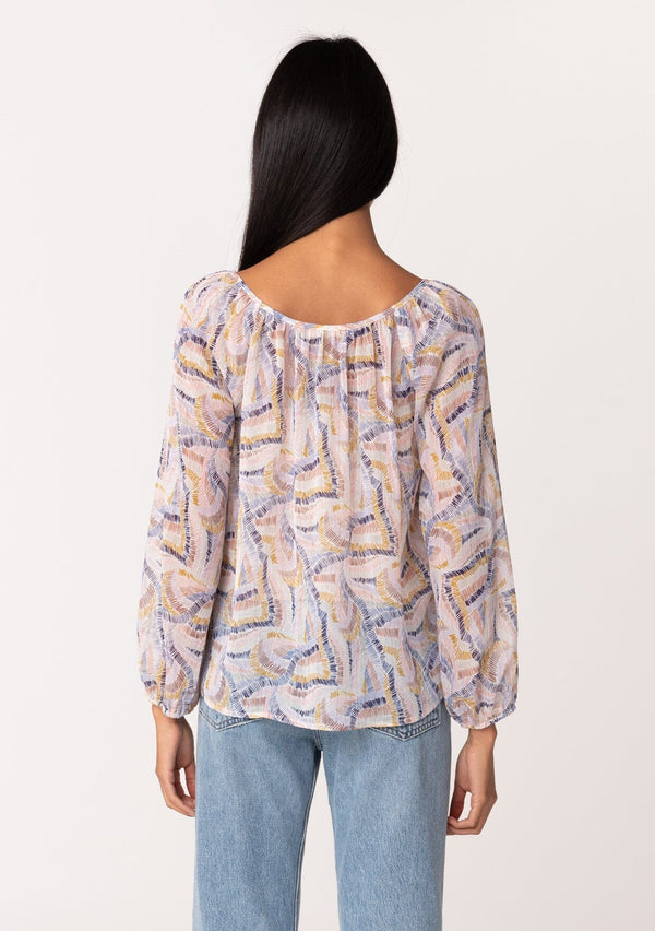 [Color: Natural/Mustard] A back facing image of a brunette model wearing a dreamy sheer chiffon fall blouse in a multi colored abstract brush stroke print. With gold metallic thread details, long sleeves, a round neckline, and a tie front accent. 