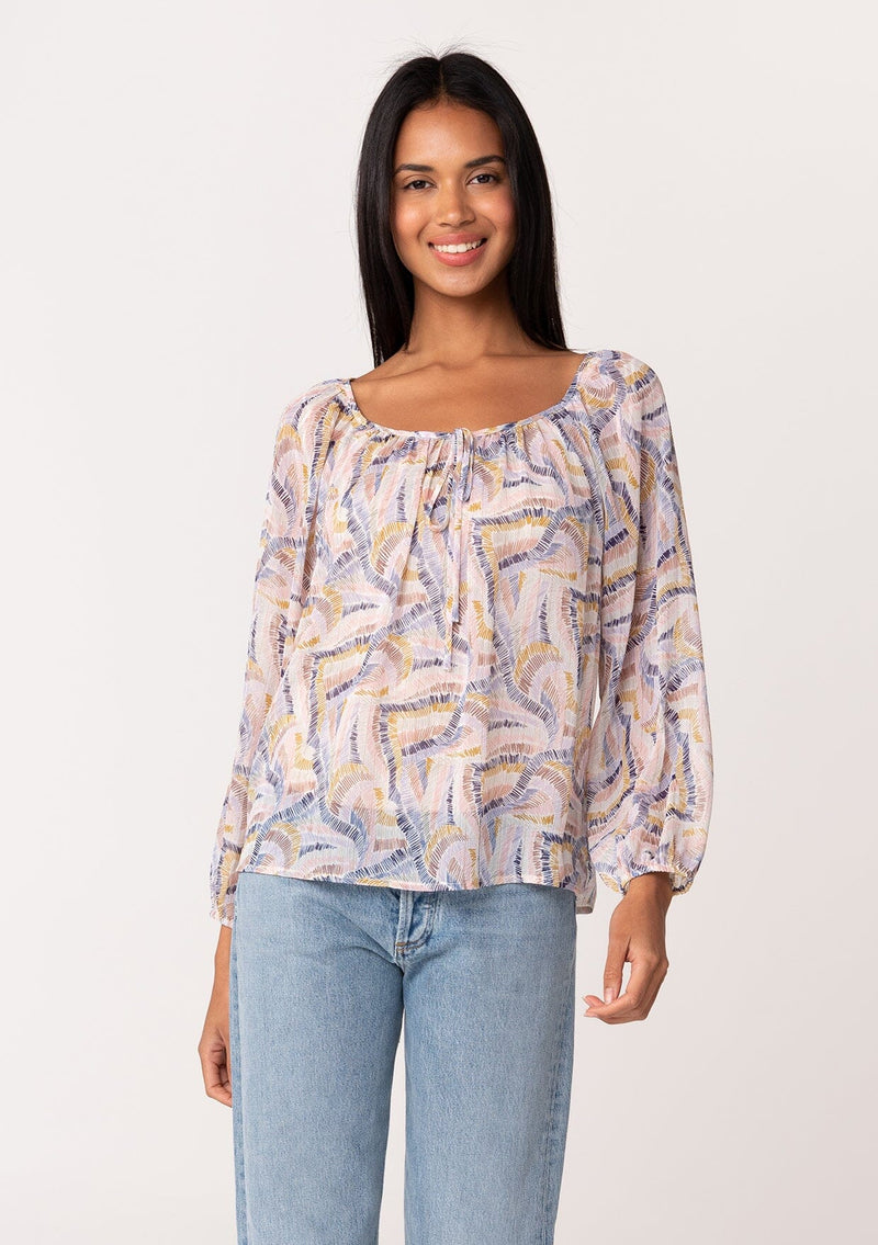 [Color: Natural/Mustard] A front facing image of a brunette model wearing a dreamy sheer chiffon fall blouse in a multi colored abstract brush stroke print. With gold metallic thread details, long sleeves, a round neckline, and a tie front accent. 