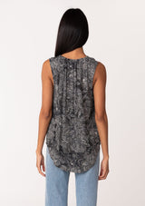 [Color: Black/Natural] A back facing image of a brunette model wearing a lightweight sleeveless blouse in a black and natural floral print. With a ruffled neckline, a split v-neckline with ties, and a relaxed fit. 