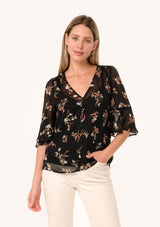 [Color: Black/Peach] A front facing image of a blonde model wearing a delicate chiffon bohemian blouse in a black and peach floral print. With half length flutter sleeves, a v neckline, and a self covered loop button front. 