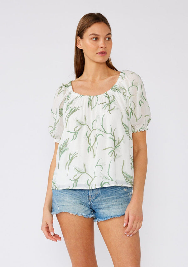 [Color: Off White/Green] A front facing image of a brunette model wearing a bohemian cotton top in a white and green embroidery. With short puff sleeves, a ruffled elastic cuff, an elastic scoop neckline, and a relaxed, flowy fit. 