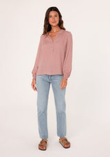 [Color: Mauve] A full body front facing image of a brunette model wearing a bohemian fall blouse in a mauve pink dot print. With long sleeves, a ruffled elastic wrist cuff, a self covered button front, a ruffled neckline, and a split v neckline.
