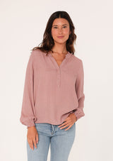 [Color: Mauve] A front facing image of a brunette model wearing a bohemian fall blouse in a mauve pink dot print. With long sleeves, a ruffled elastic wrist cuff, a self covered button front, a ruffled neckline, and a split v neckline.