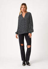 [Color: Navy] A full body front facing image of a blonde model wearing a bohemian fall blouse in a navy blue dot print. With long sleeves, a ruffled elastic wrist cuff, a self covered button front, a ruffled neckline, and a split v neckline. 