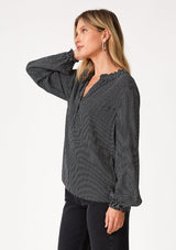 [Color: Navy] A side facing image of a blonde model wearing a bohemian fall blouse in a navy blue dot print. With long sleeves, a ruffled elastic wrist cuff, a self covered button front, a ruffled neckline, and a split v neckline. 