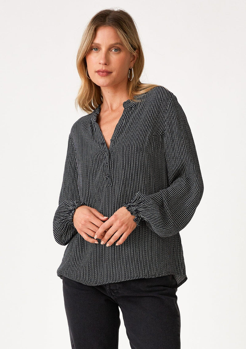 [Color: Navy] A front facing image of a blonde model wearing a bohemian fall blouse in a navy blue dot print. With long sleeves, a ruffled elastic wrist cuff, a self covered button front, a ruffled neckline, and a split v neckline. 
