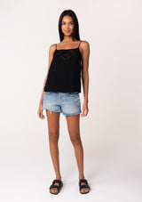 [Color: Black] A full body front facing image of a brunette model wearing a black bohemian camisole with adjustable spaghetti straps, a scoop neckline, a button up back, and lace detail. 