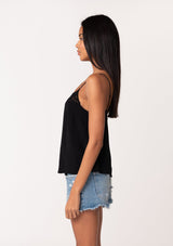 [Color: Black] A side facing image of a brunette model wearing a black bohemian camisole with adjustable spaghetti straps, a scoop neckline, a button up back, and lace detail. 