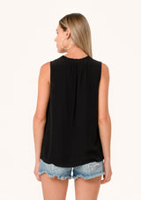 [Color: Black] A back facing image of a blonde model wearing a lightweight classic sleeveless blouse in black. With a ruffled neckline, a split v neckline with ties, and a relaxed fit.