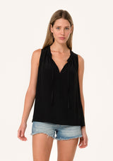 [Color: Black] A front facing image of a blonde model wearing a lightweight classic sleeveless blouse in black. With a ruffled neckline, a split v neckline with ties, and a relaxed fit.