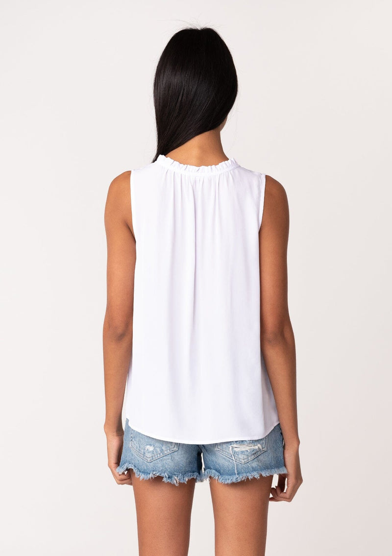 [Color: Light Lavender] A back facing image of a brunette model wearing a lightweight classic sleeveless blouse in light lavender. With a ruffled neckline, a split v neckline with ties, and a relaxed fit. 