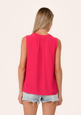 [Color: Watermelon] A back facing image of a blonde model wearing a lightweight classic sleeveless blouse in bright pink. With a ruffled neckline, a split v neckline with ties, and a relaxed fit.
