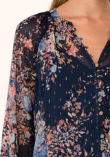 [Color: Navy/Dusty Blue] A close up front facing image of a blonde model wearing a bohemian fall blouse in a blue floral print. Designed in a metallic clip dot chiffon, with sheer long sleeves, ruffled elastic wrist cuffs, a button loop trimmed v neckline, and a self covered button front. 
