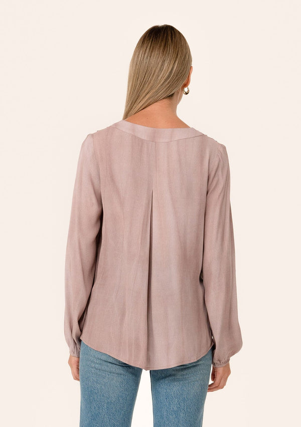 [Color: Rose Water] A back facing image of a blonde model wearing a rose pink bohemian blouse. With long sleeves, a v neckline, and pleated shoulder details. 