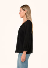 [Color: Black] A side facing image of a blonde model wearing a black bohemian fall blouse. With a v neckline, long sleeves, and embroidered detail.