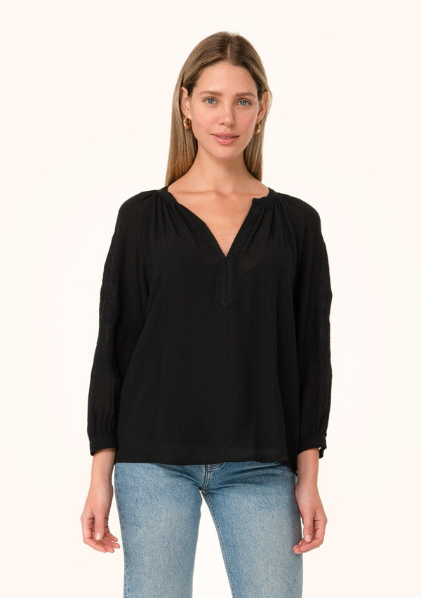 [Color: Black] A front facing image of a blonde model wearing a black bohemian fall blouse. With a v neckline, long sleeves, and embroidered detail. 