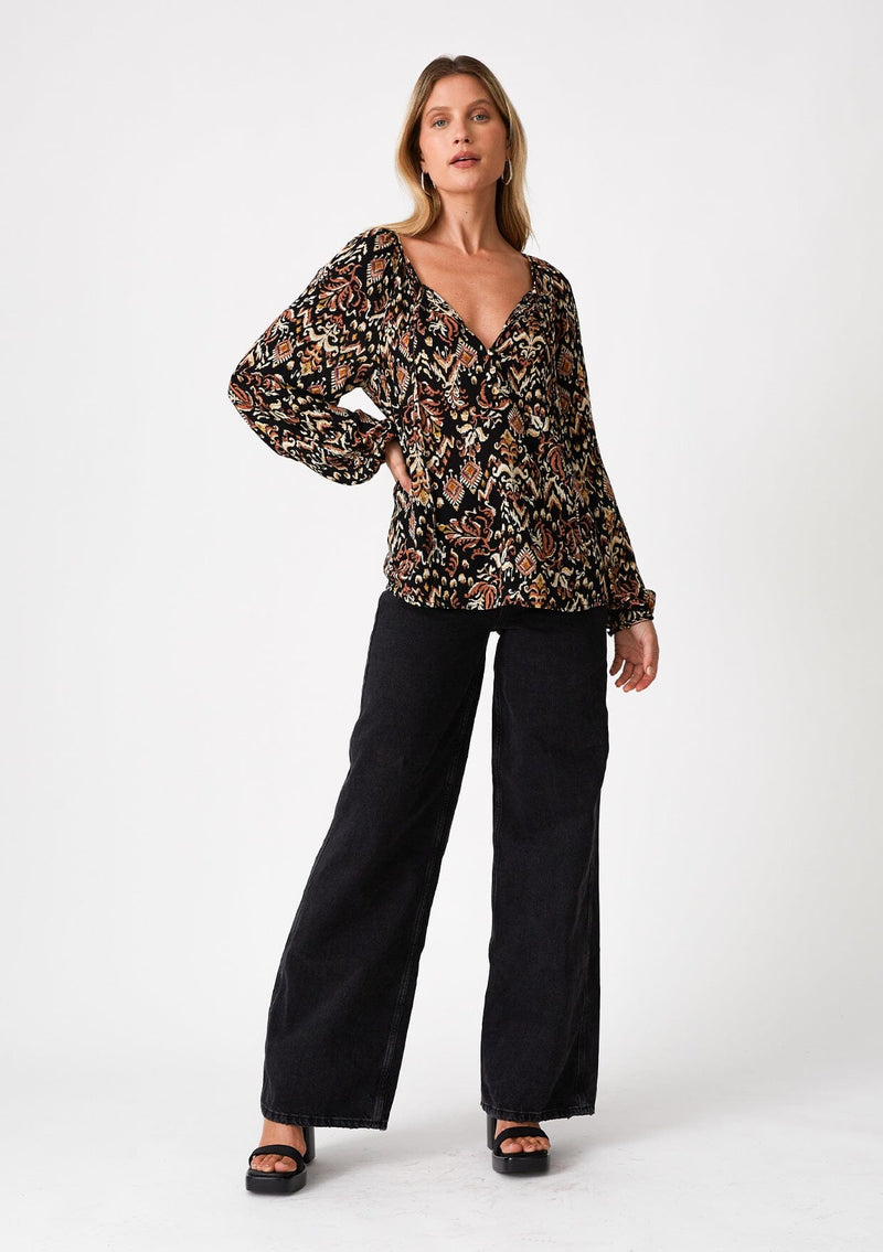 [Color: Black/Taupe] A front facing image of a blonde model wearing a flowy bohemian blouse in a brown bohemian print. With voluminous long raglan sleeves, a split v neckline with ties, and a self covered button front. 