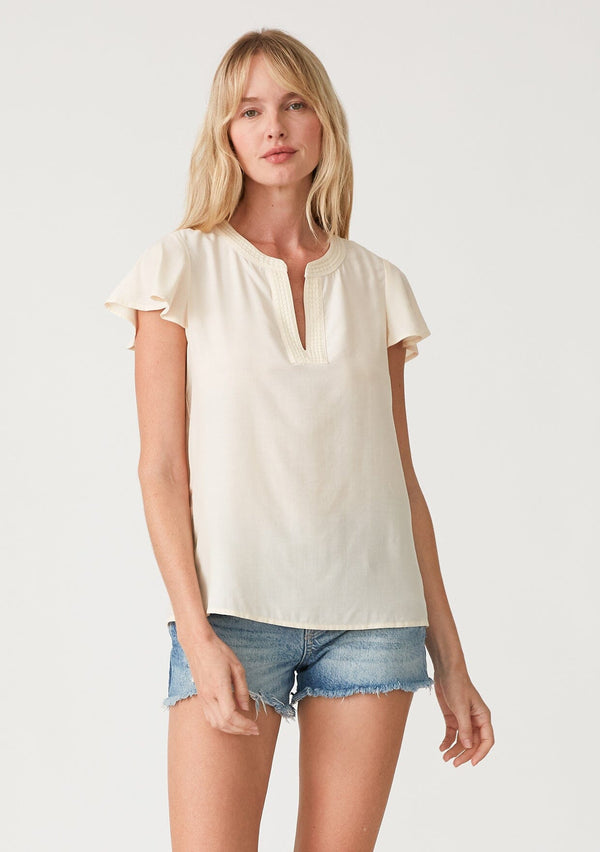 [Color: Cream] A front facing image of a blonde model wearing a lightweight bohemian resort top  in cream. With short flutter sleeves, a split v neckline with embroidered top stitch details, and a relaxed fit. 
