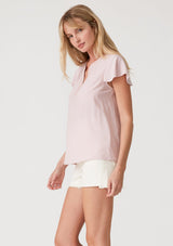 [Color: Dusty Pink] A side facing image of a blonde model wearing a lightweight bohemian resort top  in dusty pink. With short flutter sleeves, a split v neckline with embroidered top stitch details, and a relaxed fit. 