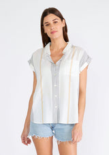 [Color: White/Gold] A half body front facing image of a brunette model wearing a lightweight short sleeve shirt designed in a textured white and black embroidered and gold metallic stripe. With short cuffed sleeves, a collared neckline, a button front, and a front patch pocket. 