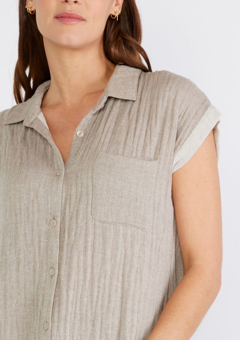 [Color: Taupe] A close up front facing image of a brunette model wearing a light brown short sleeve shirt crafted from soft cotton gauze. With a button up front, a collared neckline, a front patch pocket, and short contrast cap sleeves. 